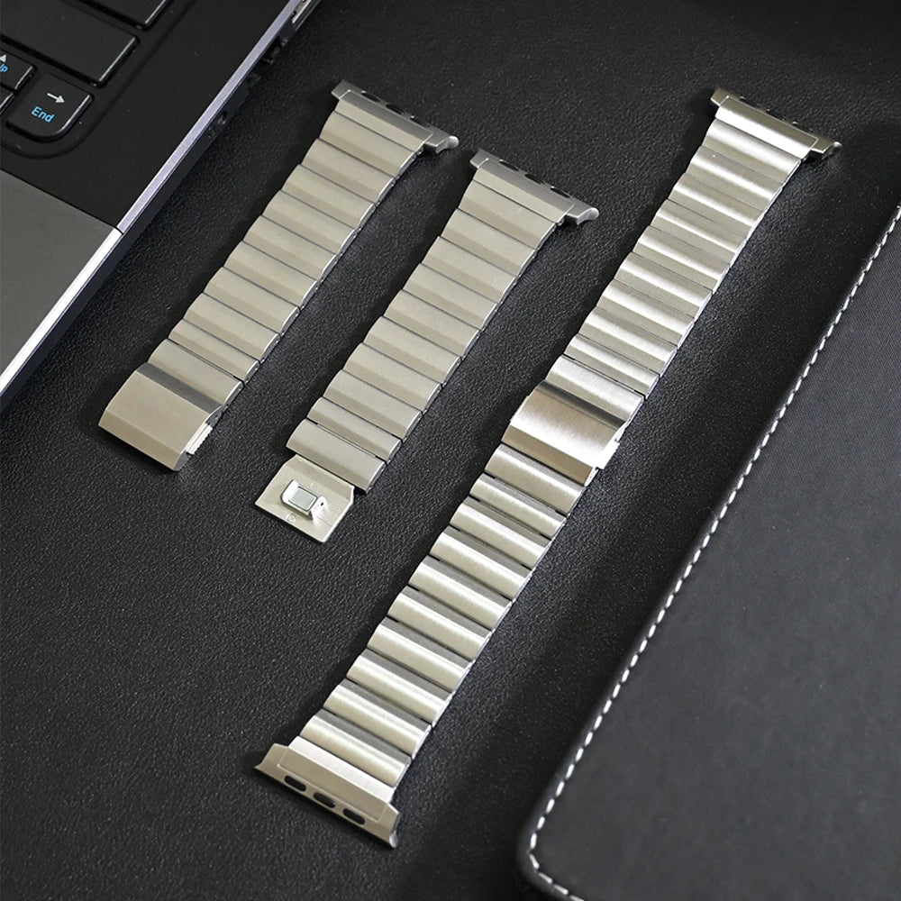 Disassembled stainless steel Apple Watch band with adjustable links, displayed on a desk. Includes tools for customization.